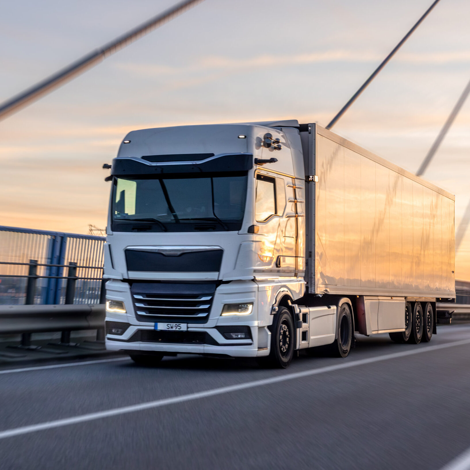 A powerful white freight truck drives over the modern bridge at golden hour. Concept of professional logistics, speed, and efficient transportation at sunset.